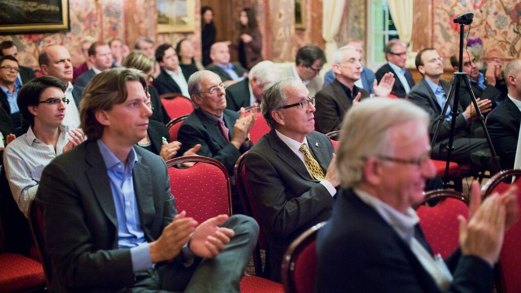Guests seated on red chairs applauding in a richly decorated salon